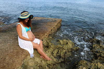 Young woman sitting on rock by sea