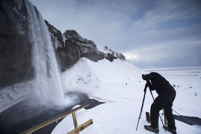 Man photographing waterfall against sky during winter