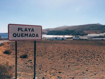 Warning sign on desert against sky