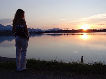 People standing on lakeshore at sunset