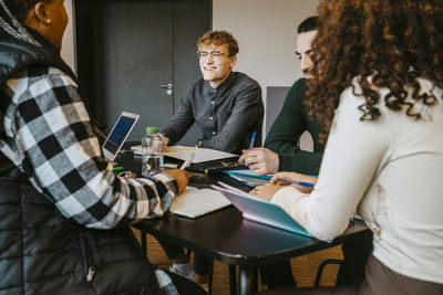 Smiling multiracial adult students studying together at table in cafeteria