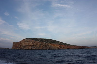 Islet or rocky cliff between the rough sea of ibiza and the blue sky in balearic islands