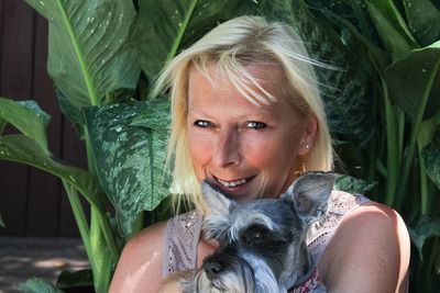 Close-up portrait of happy woman sitting with miniature schnauzer by plants