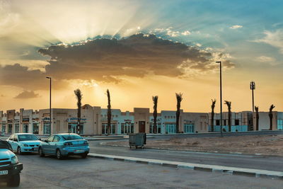 Cars on street by buildings against sky during sunset