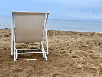 Empty chair on beach against sky