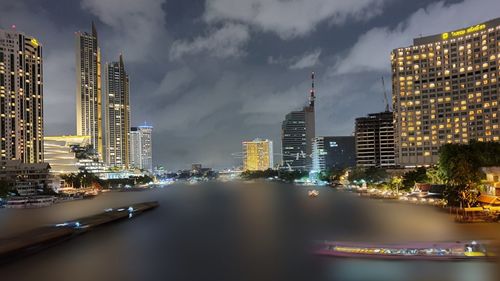 Illuminated buildings in city against cloudy sky