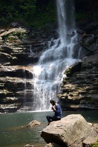 Woman sitting on cliff against waterfall