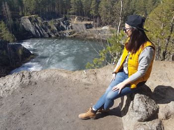 Woman sitting on rock against sky