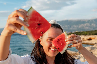 Portrait of happy young woman holding piece of watermelon in front of face.