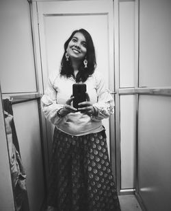 Young woman using phone while standing on mirror