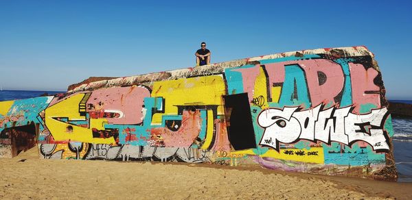 Graffiti on wall by sea against clear sky