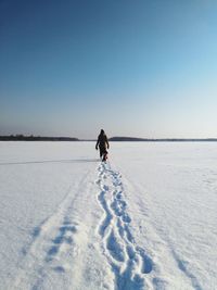 Full length of woman with dog walking on snowy field against clear sky