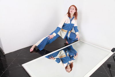 Fashion portrait of stylish woman in summer blue white stripes suit  sitting near reflecting mirror