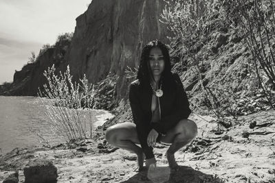 Portrait of seductive woman crouching by lake during sunny day