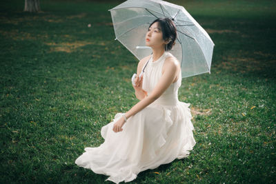 Portrait of young woman with umbrella standing on field