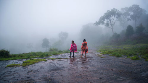 Rear view of people standing on land during rainy season