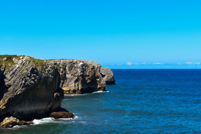 Rock formation in sea against blue sky