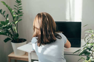 Rear view of woman sitting on table at home