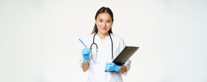 Portrait of smiling female doctor standing against white background