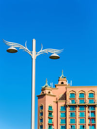 Low angle view of street light against building against clear blue sky