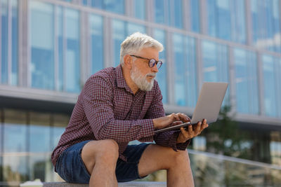 An adult man with a laptop is working outside. grey-haired european senior businessman or marketer