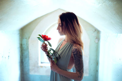 Woman holding rose while standing against white wall