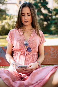 Beautiful young woman using phone while sitting on bench