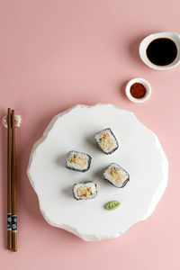 Spicy tuna roll toro maki sushi with wasabi, soy sauce, and chilli powder. on pink background