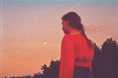 Silhouette woman standing by tree against orange sky