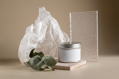 Face cream composition in a metal jar on a beige background with stone, glass and eucalyptus leaf