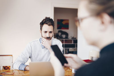 Man working on laptop while woman using mobile phone at home