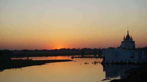 Scenic view of lake by buildings against sky during sunset