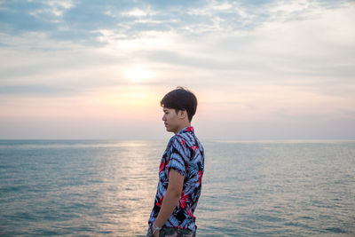 Man standing in sea against sky during sunset