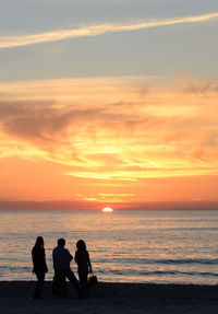 Silhouette people on beach against sky during sunset