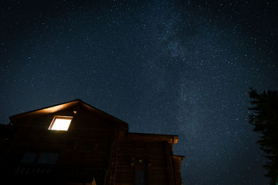 Lonely glowing window in a wooden house, silhouette against the starry sky
