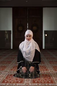 Woman in burka praying while kneeling on carpet