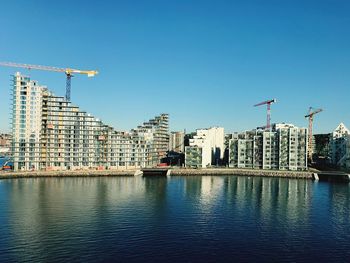 Buildings by river against clear blue sky