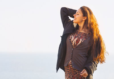 Side view of young woman standing against sky