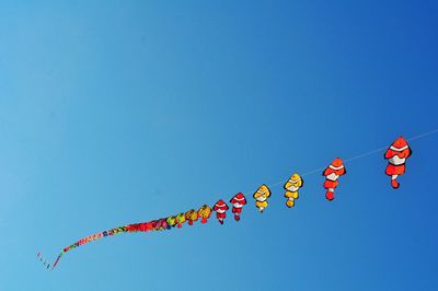 Low angle view of balloons flying against clear blue sky