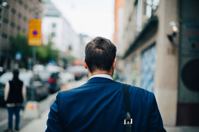 Rear view of mature businessman walking on sidewalk in city