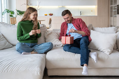 Tenderly loving female looking at boyfriend unbracing ribbon on giftbox presented for special event