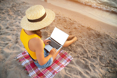 Woman using and typing on a laptop computer keyboard while sitting on a beautiful beach. mockup