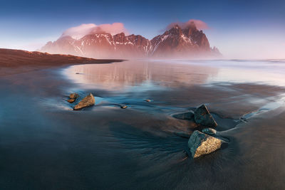 Scenic view of sea by snowcapped mountain against sky during winter