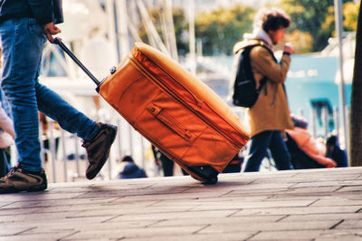 Low section of people walking with luggage on footpath