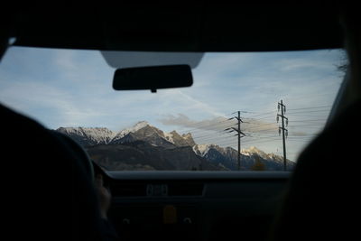 Close-up of silhouette hand against sky seen through car windshield