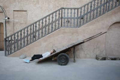 Woman lying on cart against building