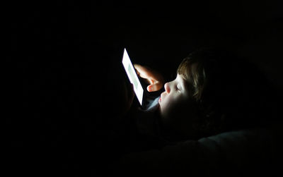 Close-up of boy using mobile phone in darkroom