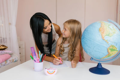 Mom helps her daughter do her homework at home. they look at each other contentedly and smile