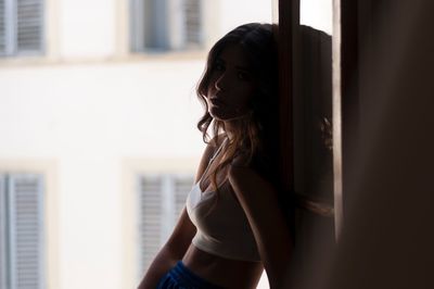 Portrait of woman standing against window at home