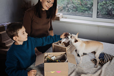 Happy family mom and kid putting bone in pet subscription box for dogs. chihuahua dog and